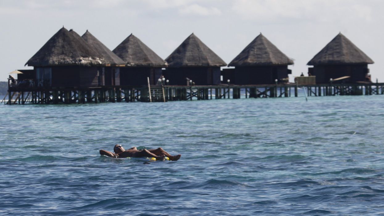 A tourist floats in front of huts at a resort island at the Male Atoll