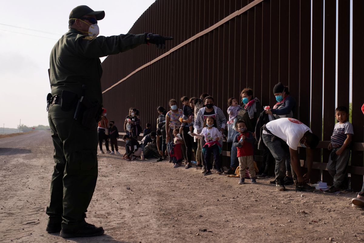 A U.S. Border Patrol agent instructs asylum-seeking migrants as they line up along the border wall after crossing the Rio Grande river into the United States from Mexico on a raft, in Penitas, Texas, U.S., March 17, 2021. 