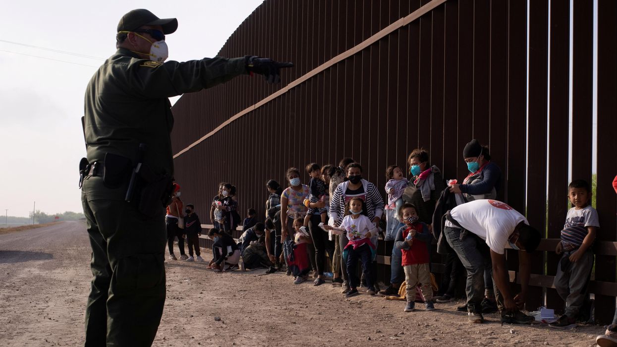 A U.S. Border Patrol agent instructs asylum-seeking migrants as they line up along the border wall after crossing the Rio Grande river into the United States from Mexico on a raft, in Penitas, Texas, U.S., March 17, 2021.