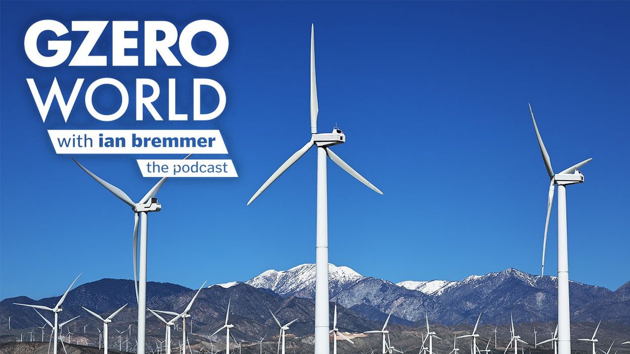 A wind farm in front of a blue sky and mountains with the GZERO World podcast logo superimposed on top.