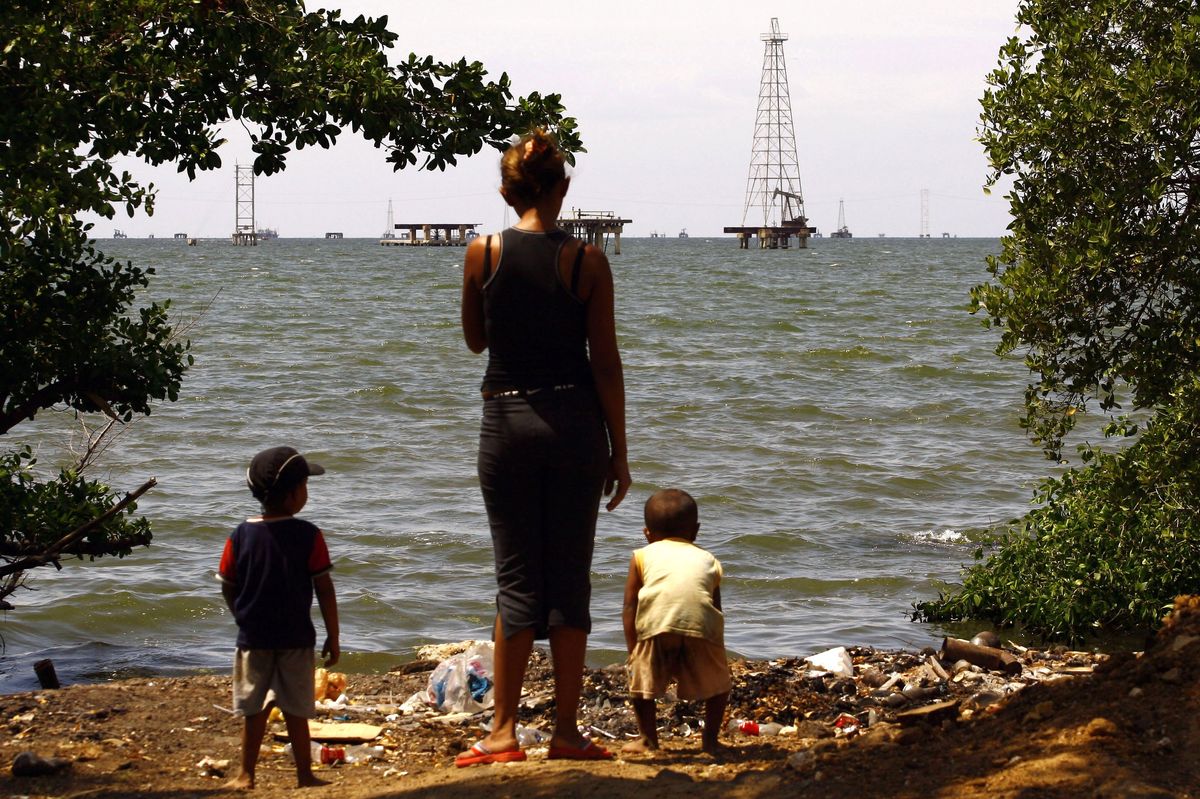 A woman and her sons stand on the edge of Maracaibo lake in front of oil rigs in Maracaibo February 15, 2008. 