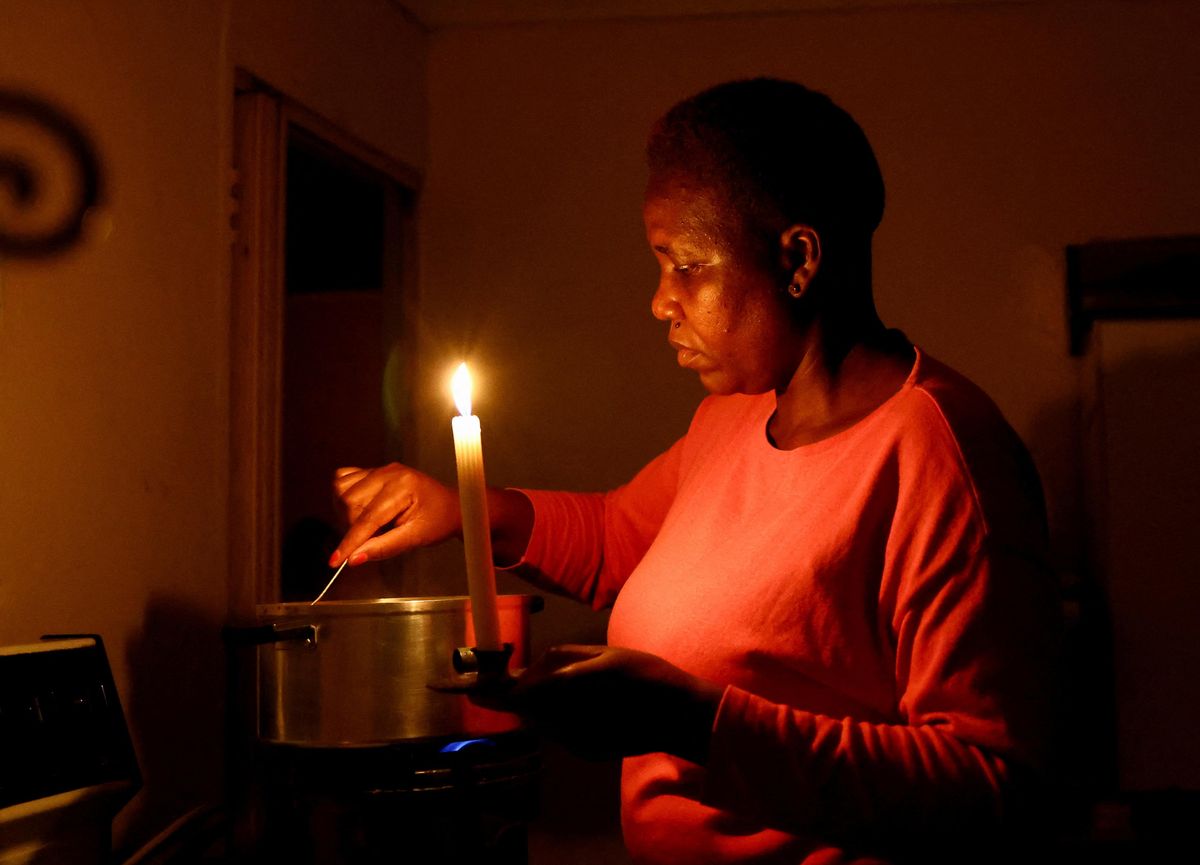 A woman cooks by a candlelight during one of the frequent power outages in South Africa. 