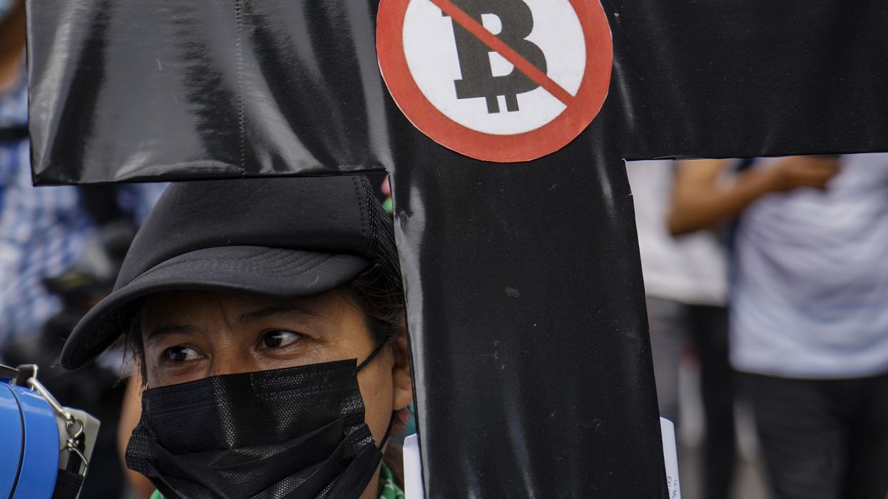 A woman holds a black cross with a sign against Bitcon during a protest against President Bukele's government in El Salvador.