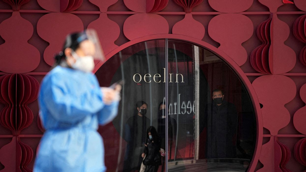 A woman in a protective suit walks past a shop as COVID outbreaks continue in Shanghai, China.
