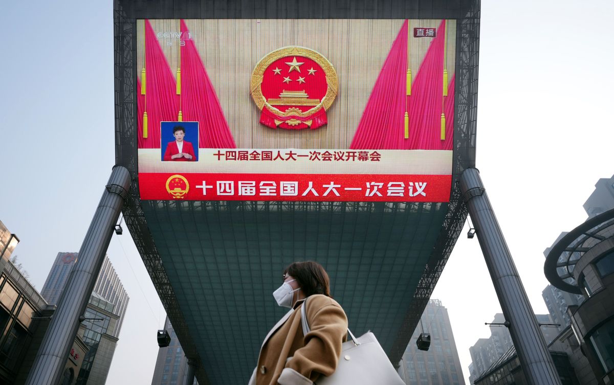 A woman passes by a giant monitor showing the "Two Sessions" in Beijing, China.