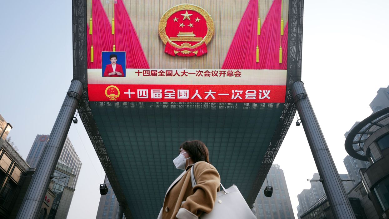 A woman passes by a giant monitor showing the "Two Sessions" in Beijing, China.