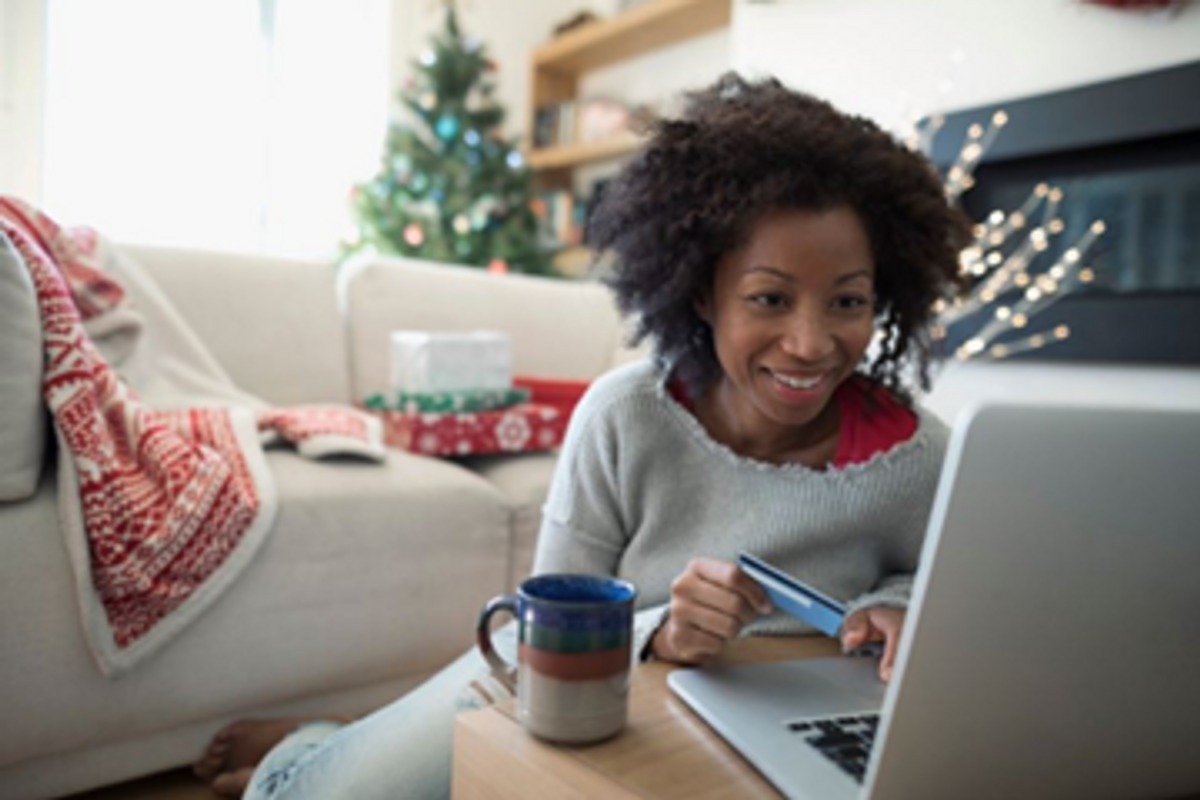 A woman sits at home in front of her laptop with a credit card in hand with holiday decorations behind her