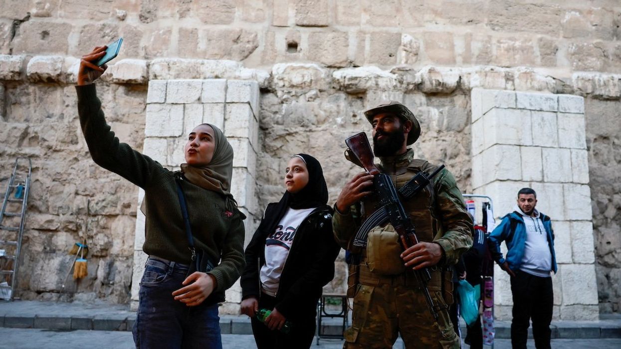 A woman uses a phone next to a fighter of the ruling Syrian body, after members of the ruling Syrian body ousted Syria's Bashar al-Assad, in the Damascus old city, Syria, December 12, 2024.
