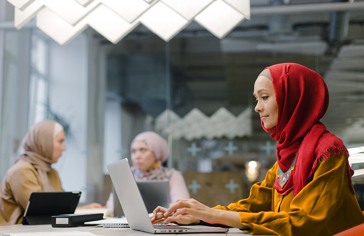 A woman wearing a head scarf uses a laptop computer at a cafe