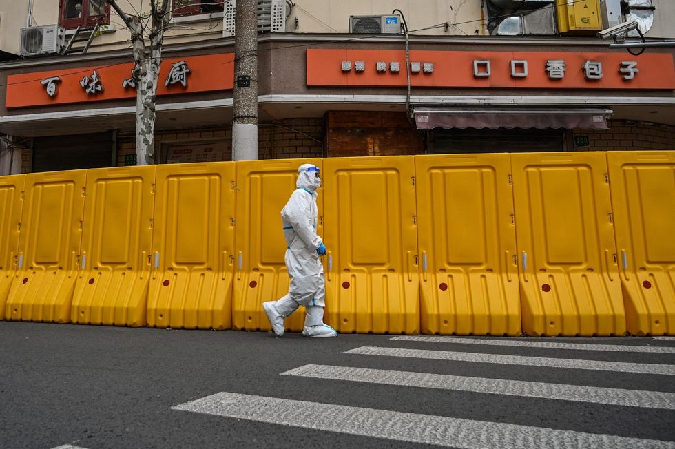 A worker wearing protective gear walks next to barriers that separate from the street a neighborhood in lockdown as a measure against Covid-19. 