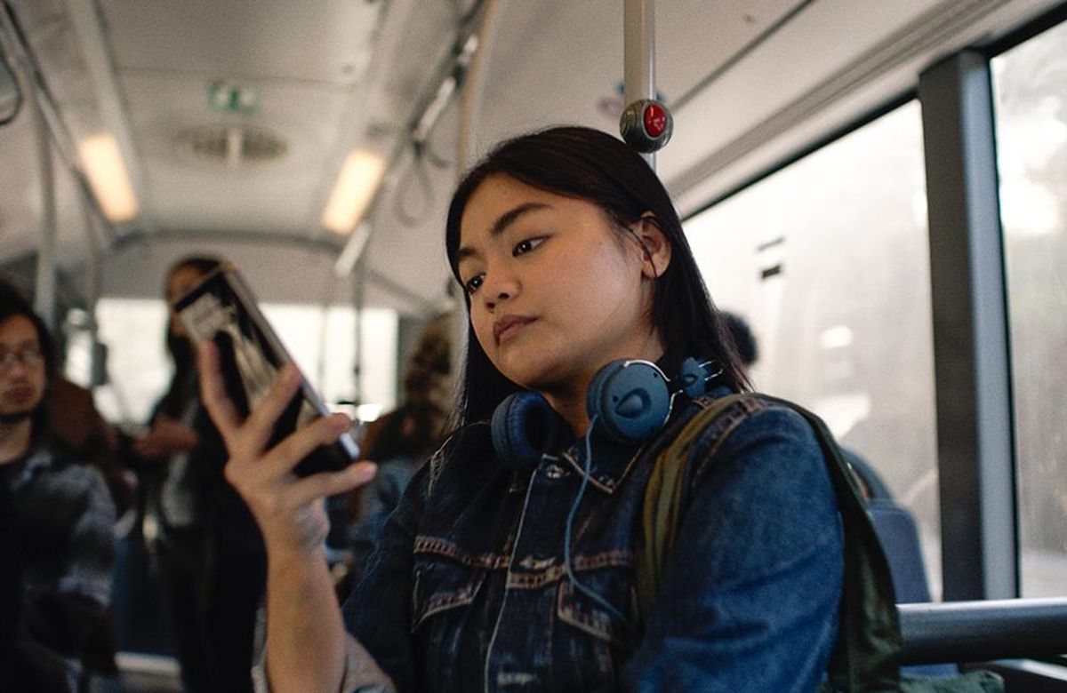 A young woman wearing headphones looking at her smartphone while riding public transportation
