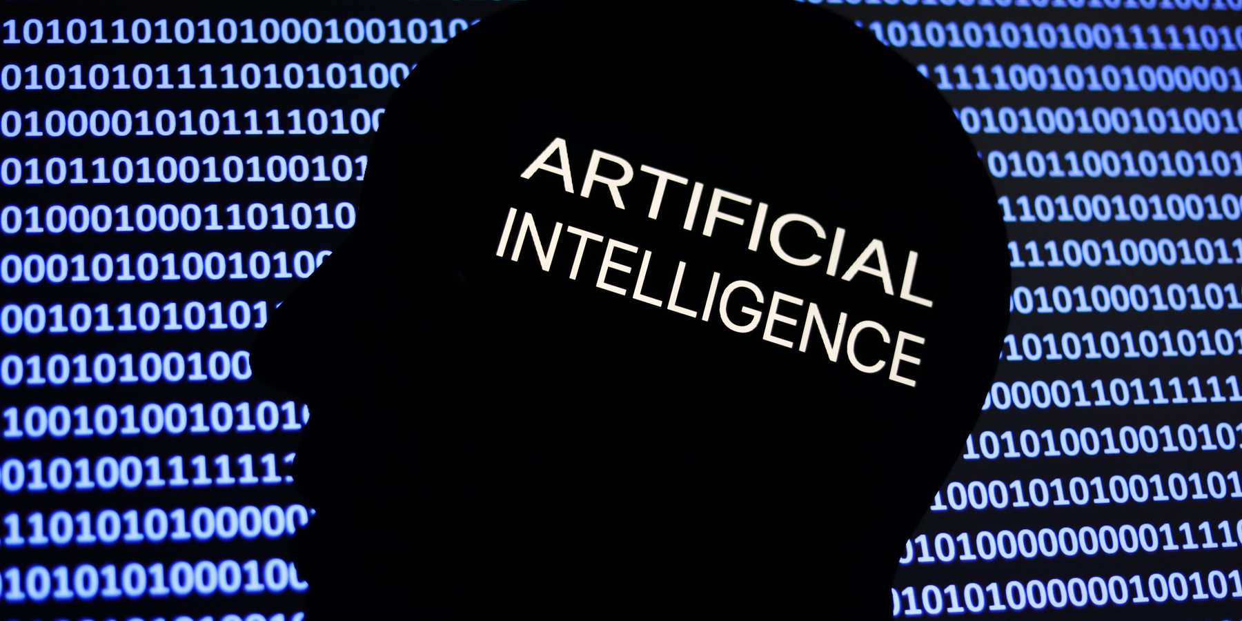 An artificial intelligence sign is displayed on a phone screen, with the shape of a human face and binary code in an illustration. 