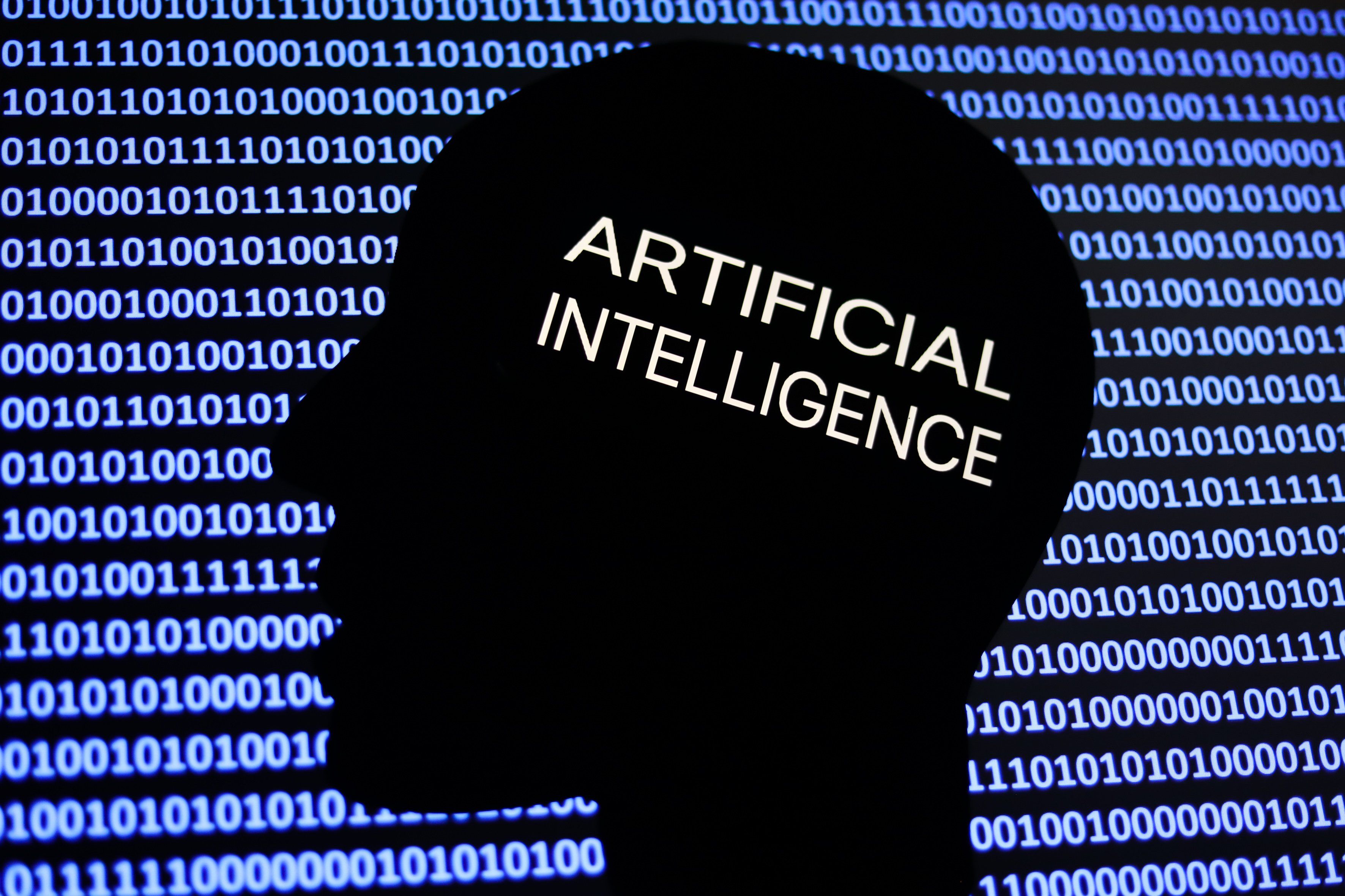 An artificial intelligence sign is displayed on a phone screen, with the shape of a human face and binary code in an illustration. 