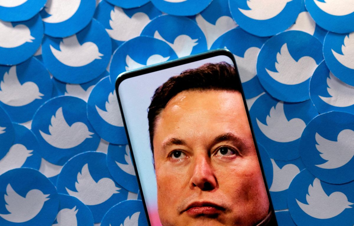 An image of Elon Musk is seen on a smartphone placed on printed Twitter logos.