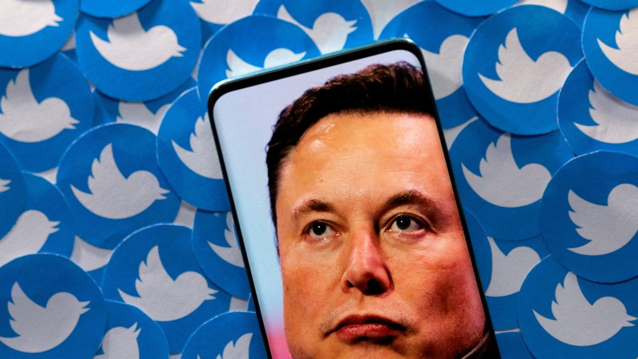 An image of Elon Musk is seen on a smartphone placed on printed Twitter logos.
