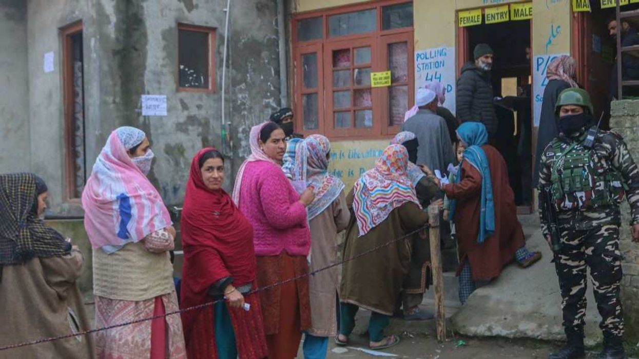 An Indian security personnel stands guard as women voters queue to cast their ballots at a polling station during the Budgam Assembly constituency bypoll in Budgam district, Jammu and Kashmir, on November 11, 2025.