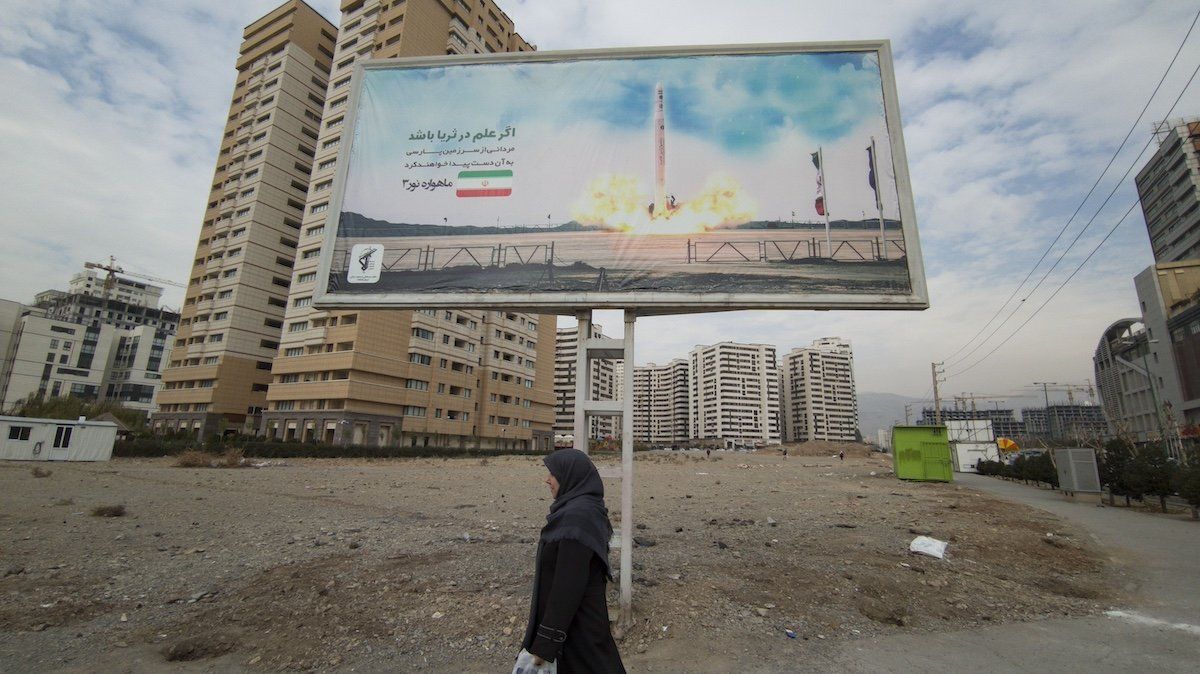 An Iranian woman is walking under a billboard that is displaying an image of the Iranian Qased satellite carrier in a residential area in northwestern Tehran, Iran, on December 13, 2023.