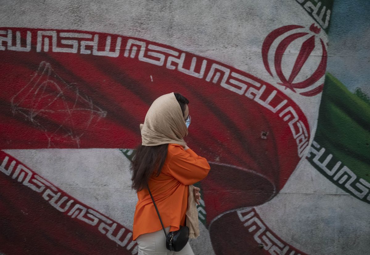 An Iranian woman walks past a huge mural of Iran's flag, in the Enghelab (Revolution) avenue in downtown Tehran, September 12, 2023.