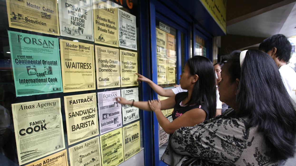Applicants looking at job offers displayed on a glass window of a recruitment agency in Manila, Philippines.