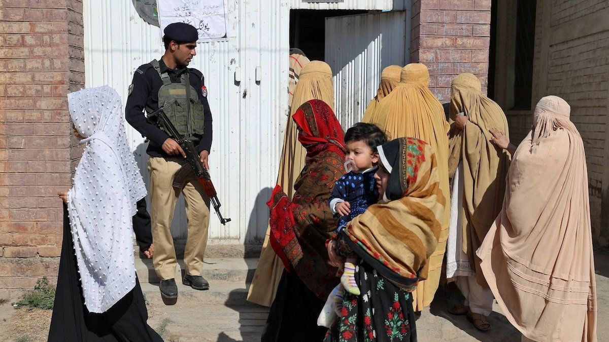 Burqa-clad women arrive at a polling station to cast their vote as a police officer stands guard during general election, in Peshawar, Pakistan, February 8, 2024.