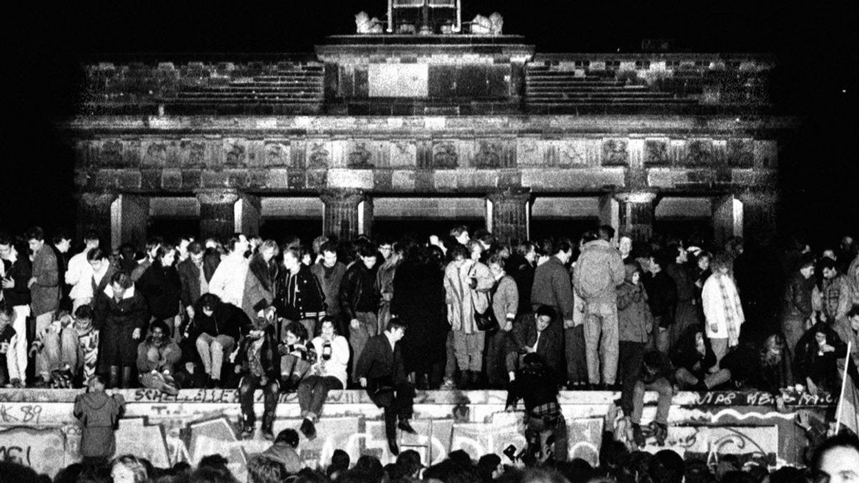 East and West German citizens celebrate as they climb the Berlin Wall after the opening of the East German border was announced, on November 9, 1989.