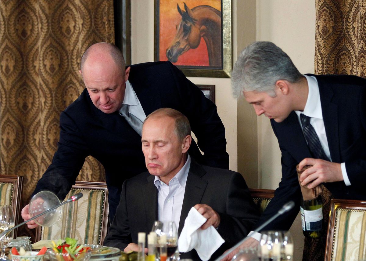Evgeny Prigozhin (L) assists Russian President Vladimir Putin