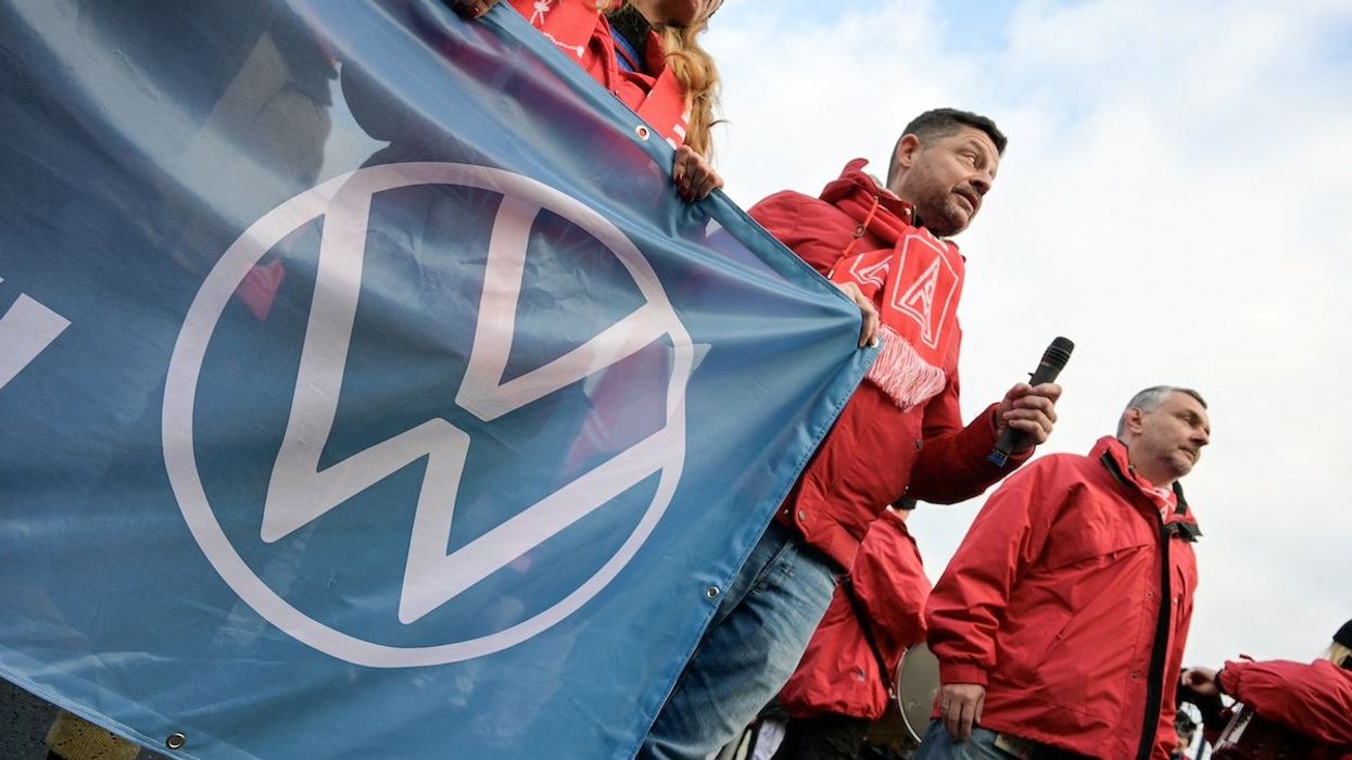 FILE PHOTO: A man wearing an IG Metall (Industrial Union of Metalworkers) scarf holds a banner with the Volkswagen logo, as workers gather to strike against planned cuts to wages and possible factory closures, in Hanover, Germany, December 2, 2024. Picture taken with long exposure.