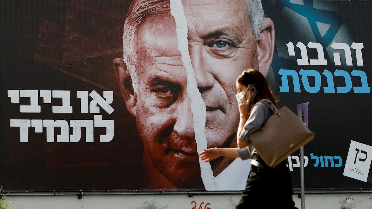 FILE PHOTO: A woman walks past a Blue and White party election campaign banner depicting its leader, Israeli Defence Minister Benny Gantz, alongside Israeli Prime Minister Benjamin Netanyahu ahead of the March 23 ballot, in Tel Aviv, Israel March 14, 2021.