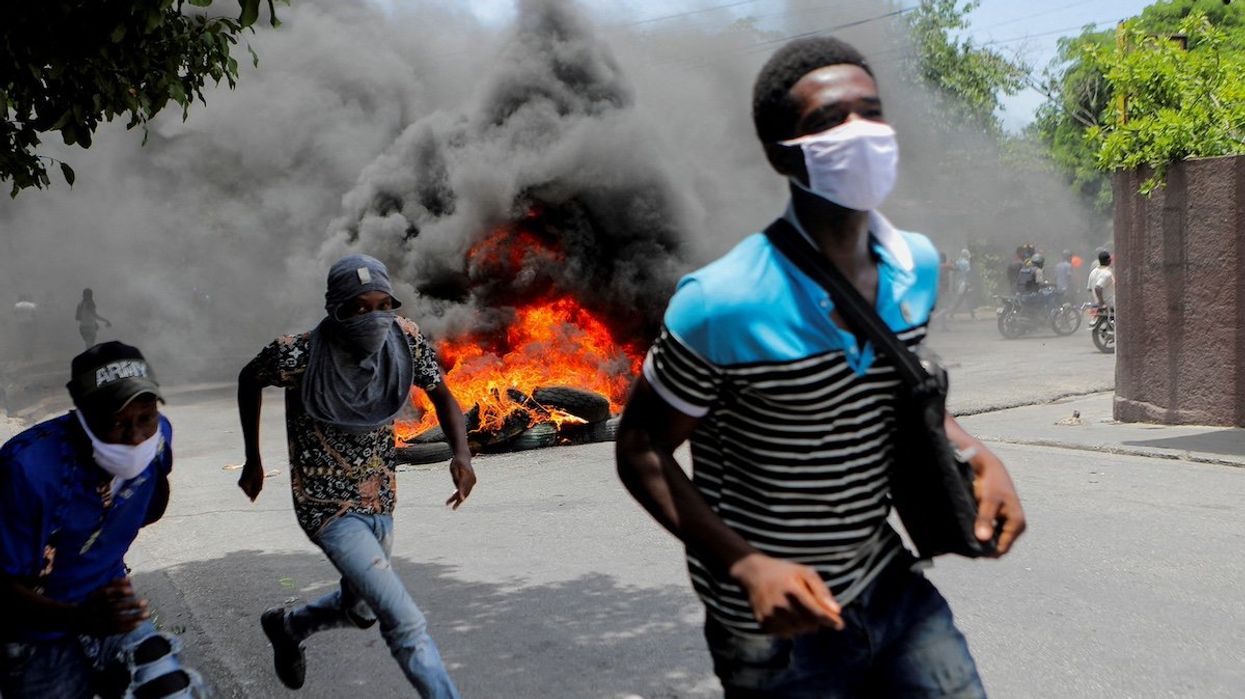 FILE PHOTO: Men run next to burning tires during a protest demanding an end to gang violence, in Port-au-Prince, Haiti, August 14, 2023.