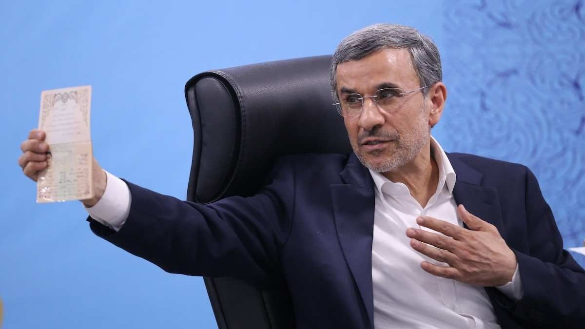 ​Former Iranian President Mahmoud Ahmadinejad showing his identity document with the other hand on his heart