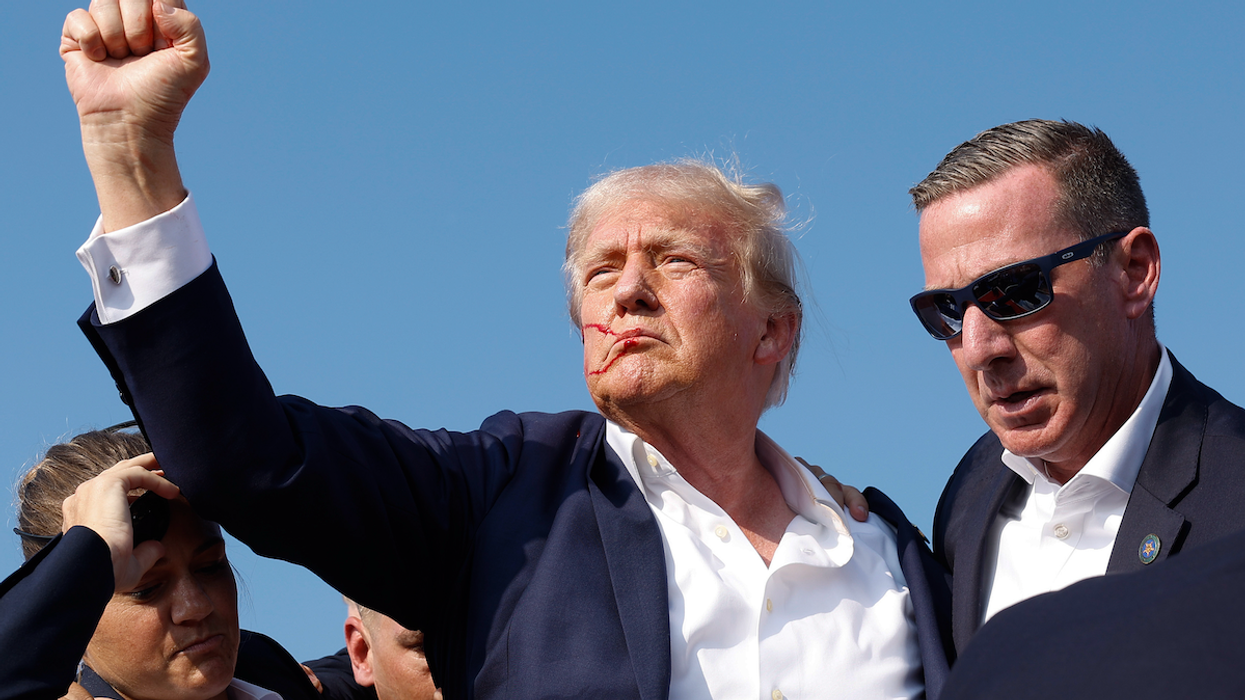 Former President Donald Trump, with his face bloodied by a shot that hit his right ear, raises his fist as he's rushed from a rally stage in Butler, PA.