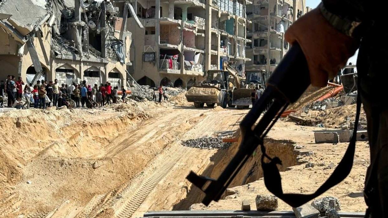 Hamas militant stands guard, as heavy machinery operates at the site where searches are underway for the bodies of hostages killed after being seized by Hamas during the October 7, 2023 attack, amid a ceasefire between Israel and Hamas, in Khan Younis, southern Gaza Strip, October 17, 2025.