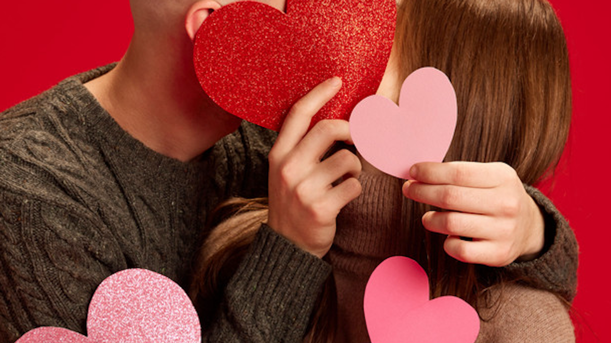 Happy young couple hide behind paper hearts to kiss.
