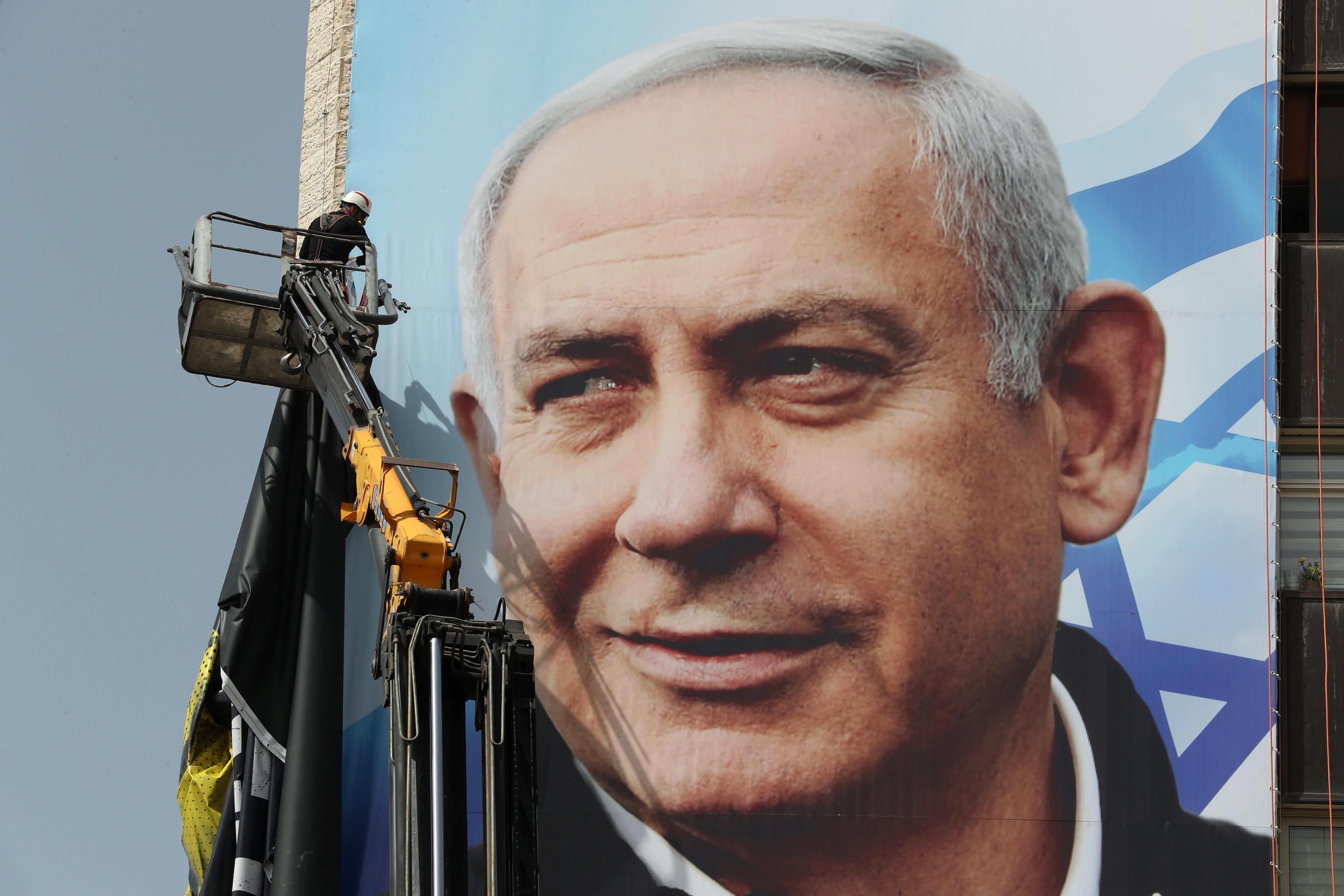 A labourer hangs a Likud party election campaign banner depicting party leader Israeli Prime Minister Benjamin Netanyahu, ahead of a March 23 ballot, in Jerusalem March 10, 2021.