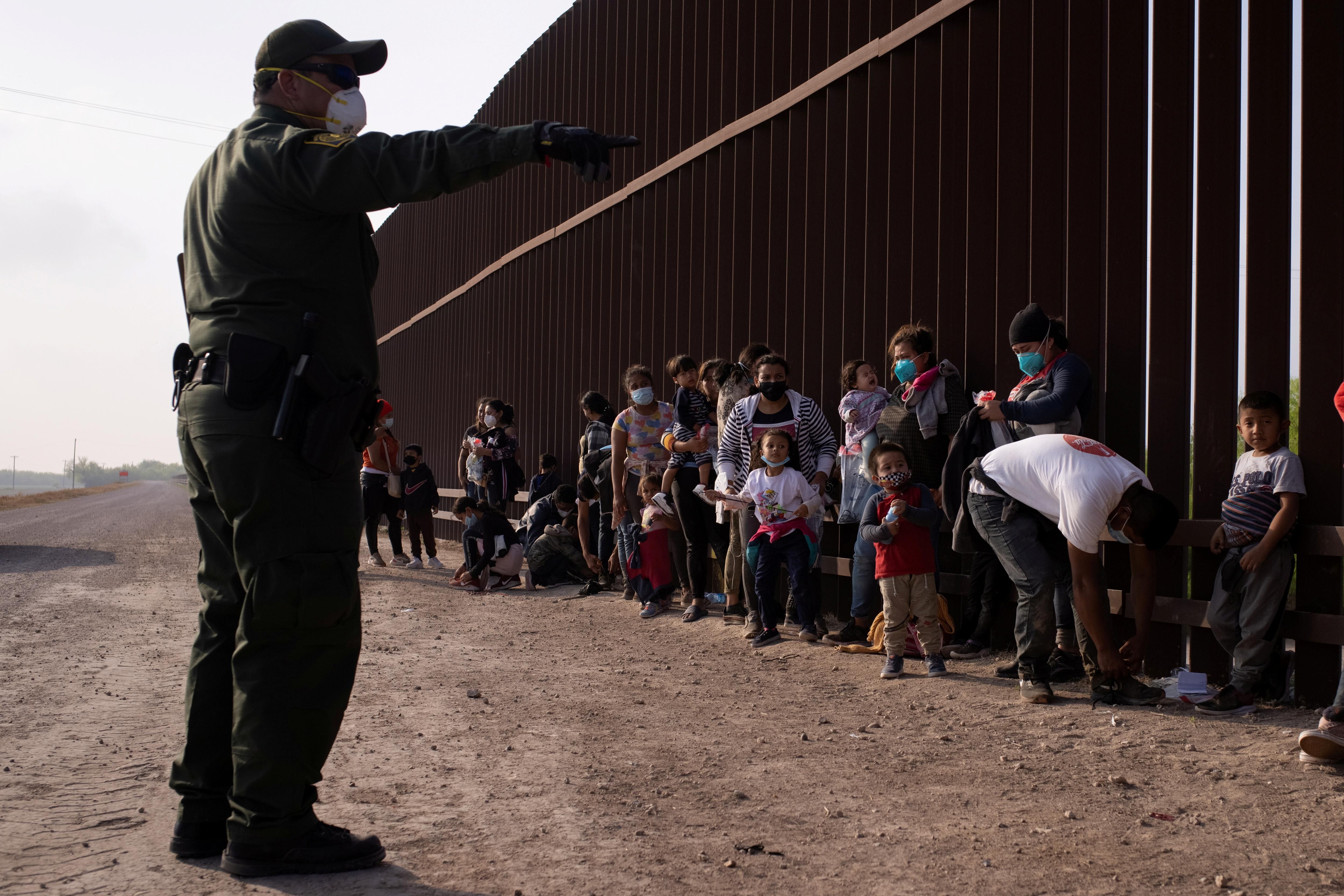 A U.S. Border Patrol agent instructs asylum-seeking migrants as they line up along the border wall after crossing the Rio Grande river into the United States from Mexico on a raft, in Penitas, Texas, U.S., March 17, 2021. 