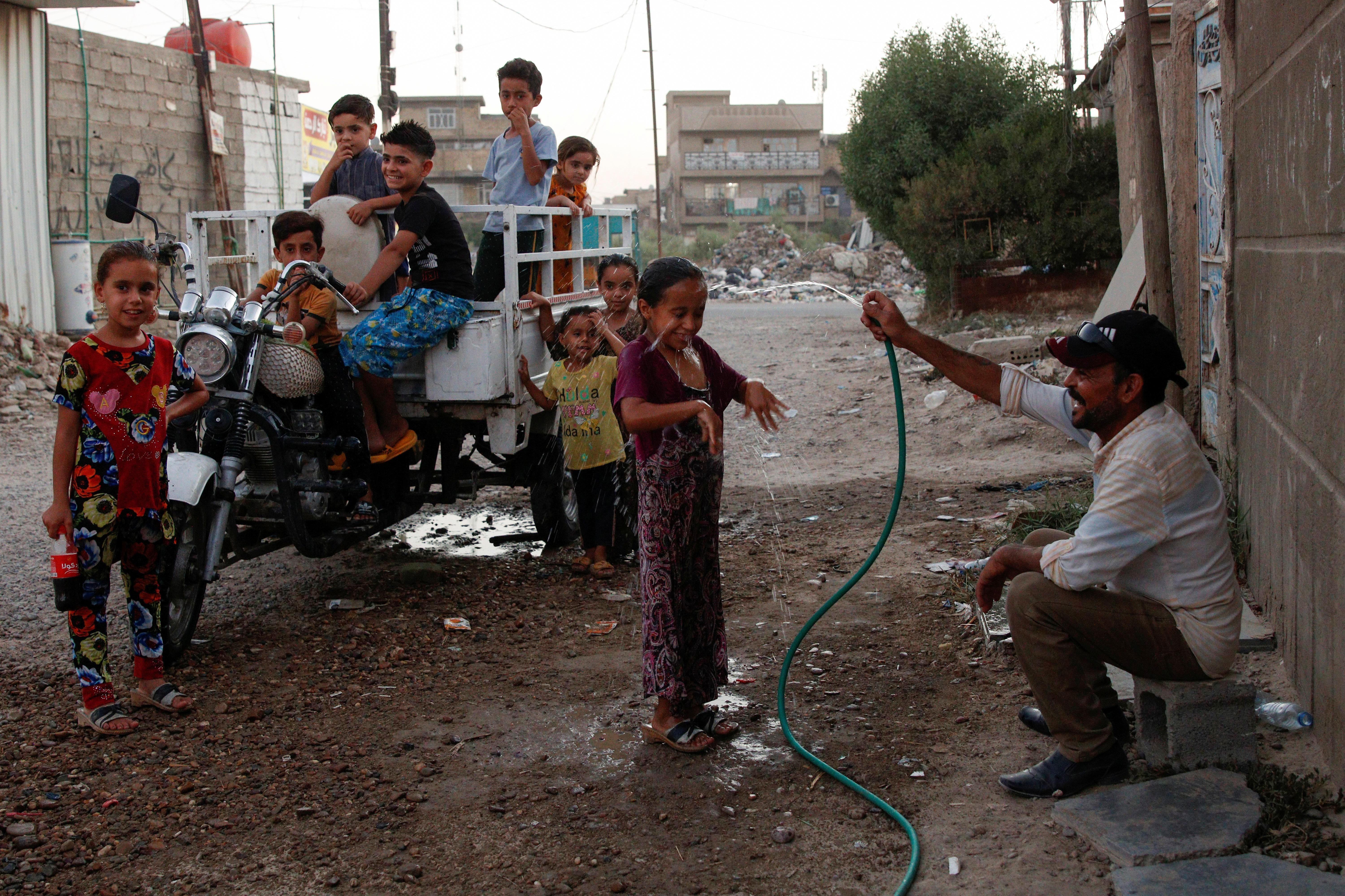 An Iraqi man sprays water on a girl in the street during a high temperature and power cut in Baghdad, Iraq July 3, 2021. Picture taken July 3, 2021