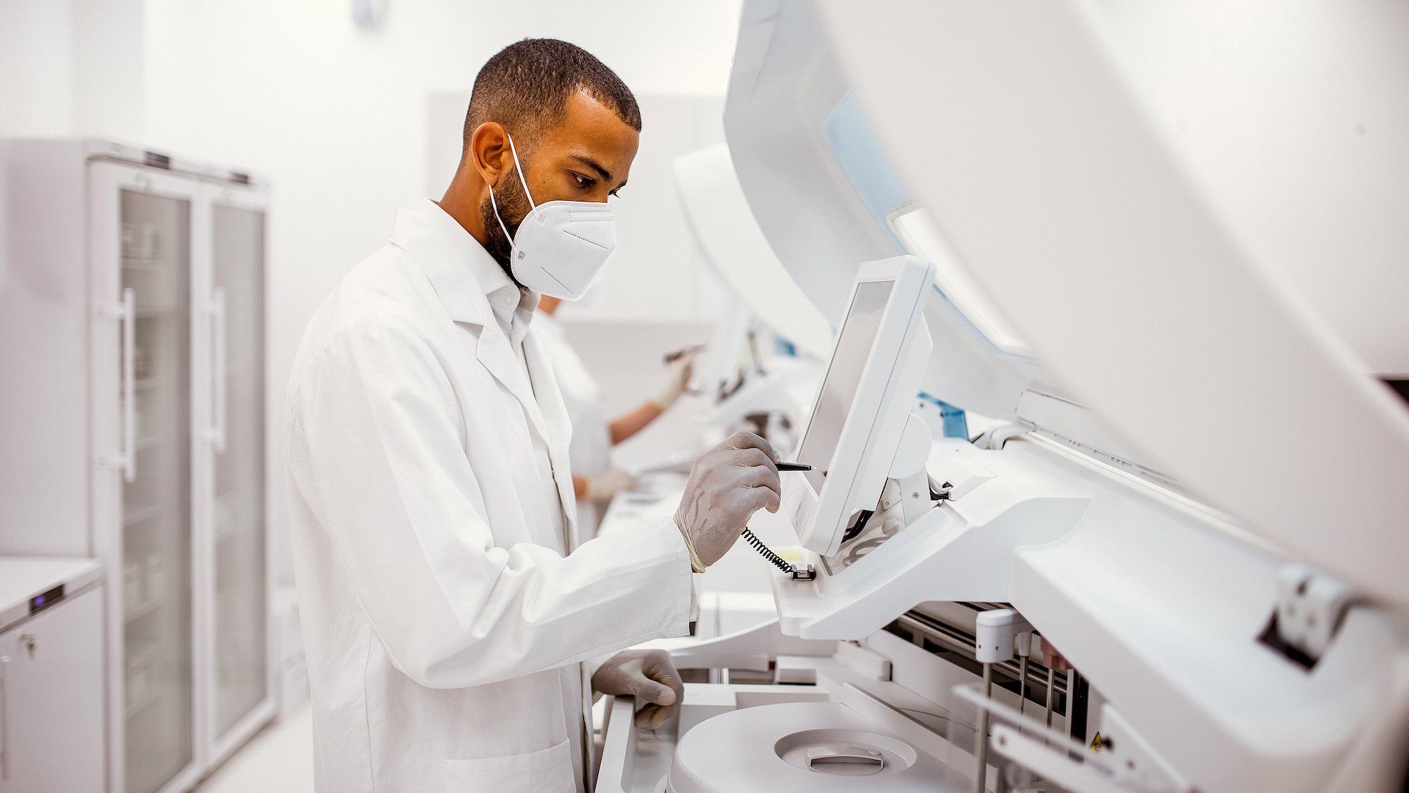A masked scientist in a high-tech white lab doing medical research.