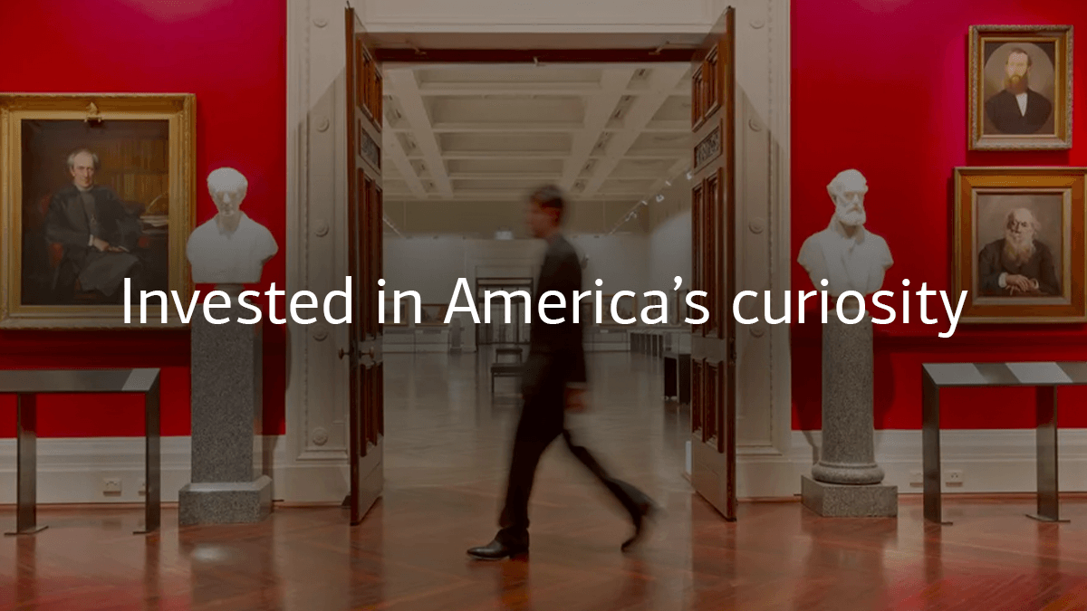 Person walking in a museum with "Invested in America's curiosity" written in the centre of the image