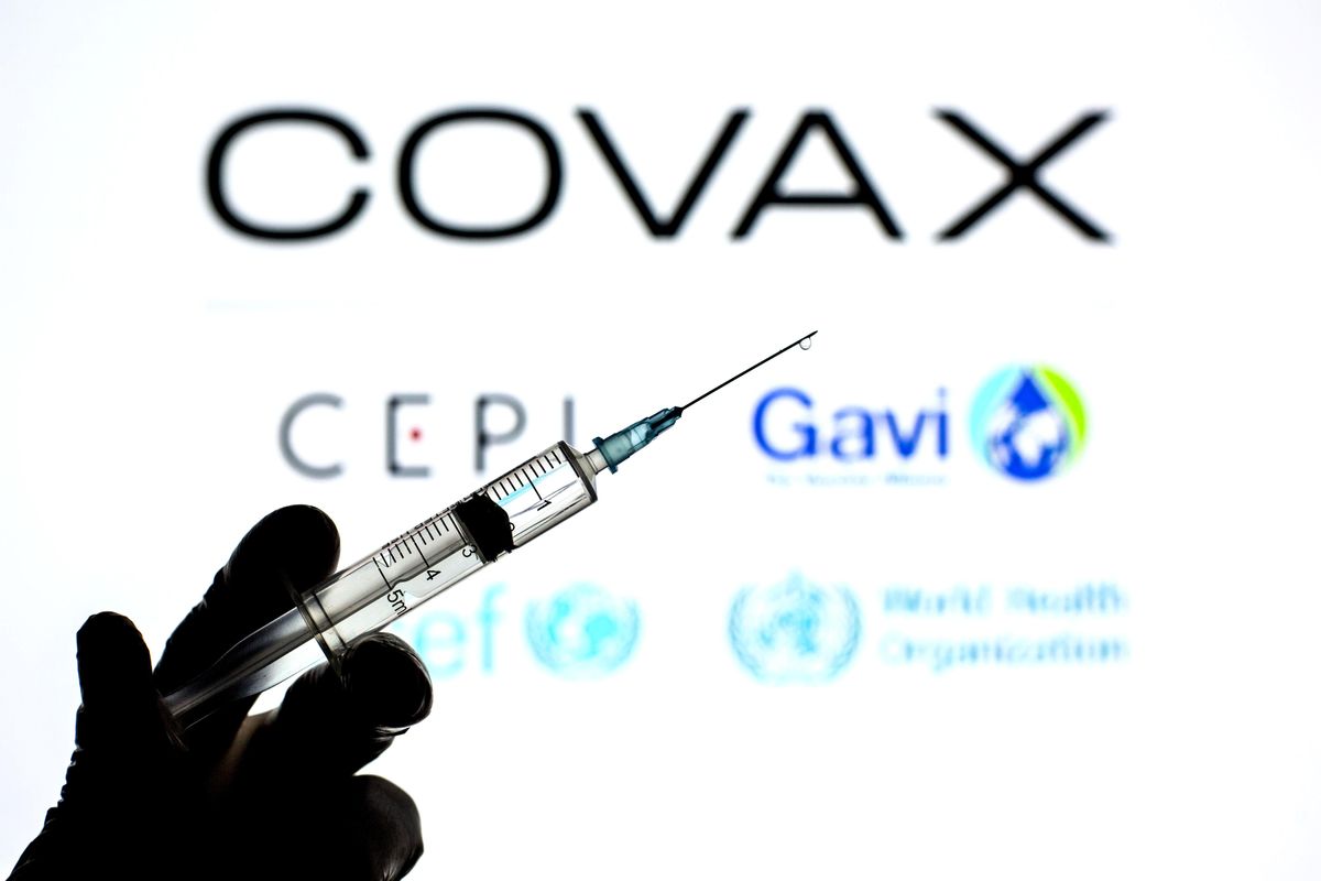 In this photo illustration a hand holding a medical syringe seen in front of the Covax Facility logo.