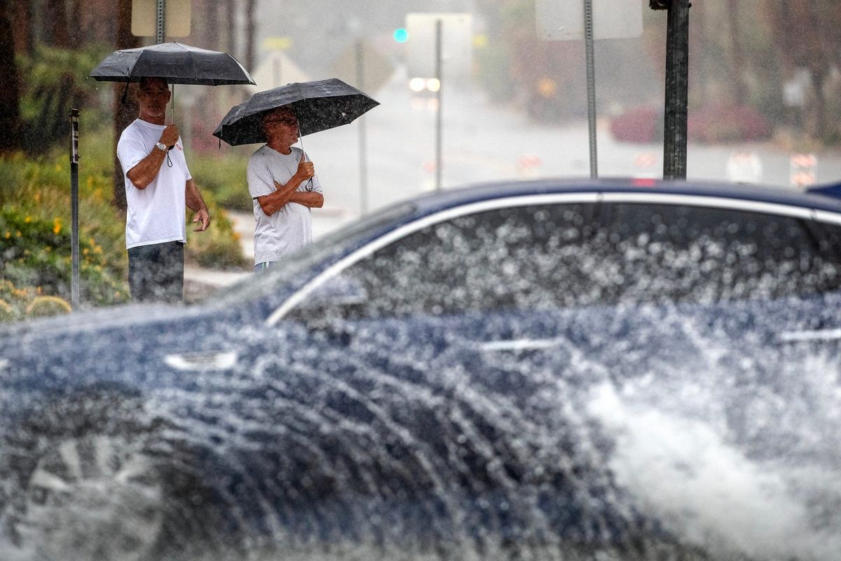 Jeff Larsen, left, and Robbie Jones watch cars drive on flooded streets during Tropical Storm Hilary in Palm Springs, Calif., on Sunday.