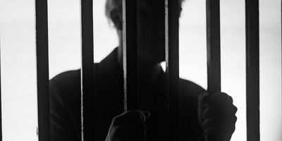 A man standing behind bars in a jail cell silhouetted.