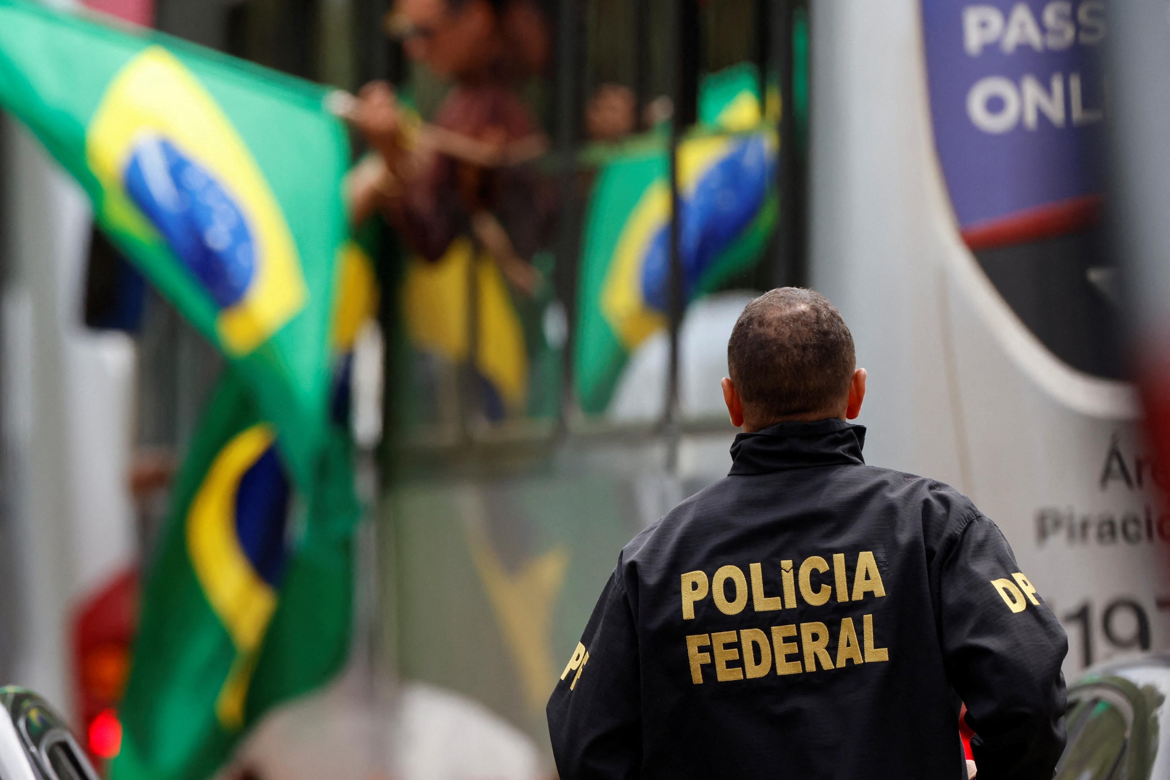 A member of the Federal Police looks on as supporters of Brazil's former President Jair Bolsonaro arrive on a bus after their camp was dismantled in Brasilia.