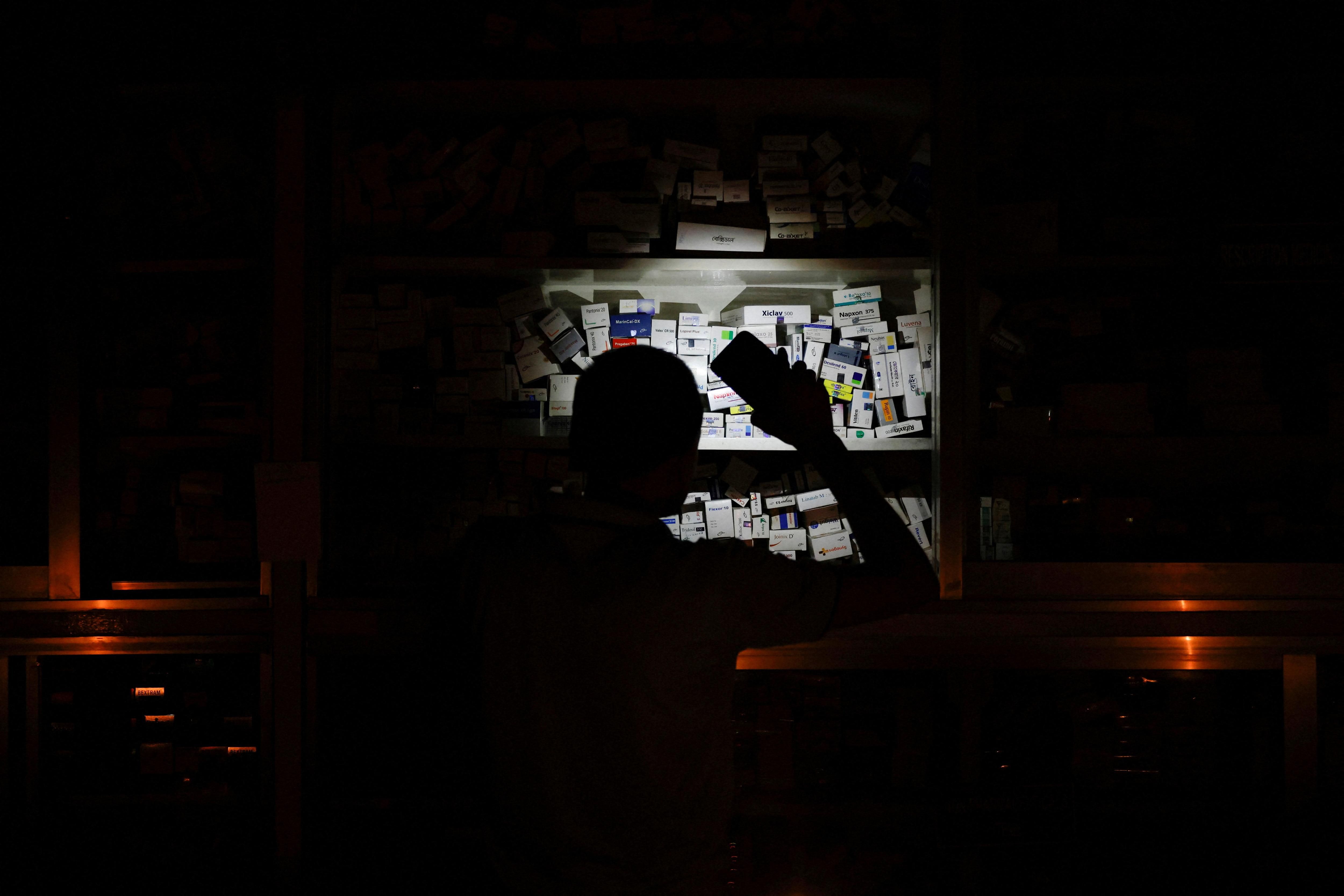 A pharmacist uses his phone light to serve customers during a nationwide blackout in Dhaka.