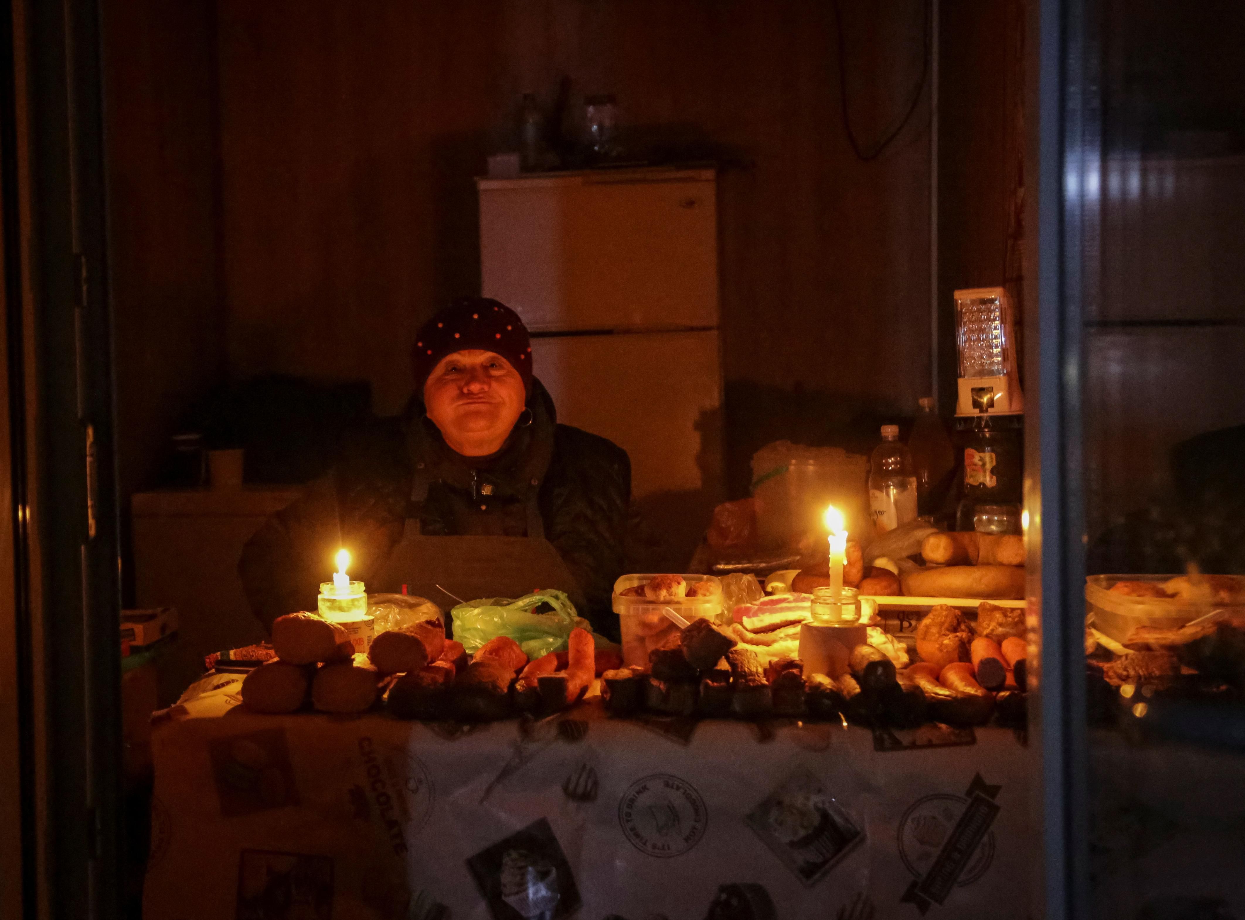 A vendor waits for customers in a small store that is lit with candles during a power outage in Odesa.