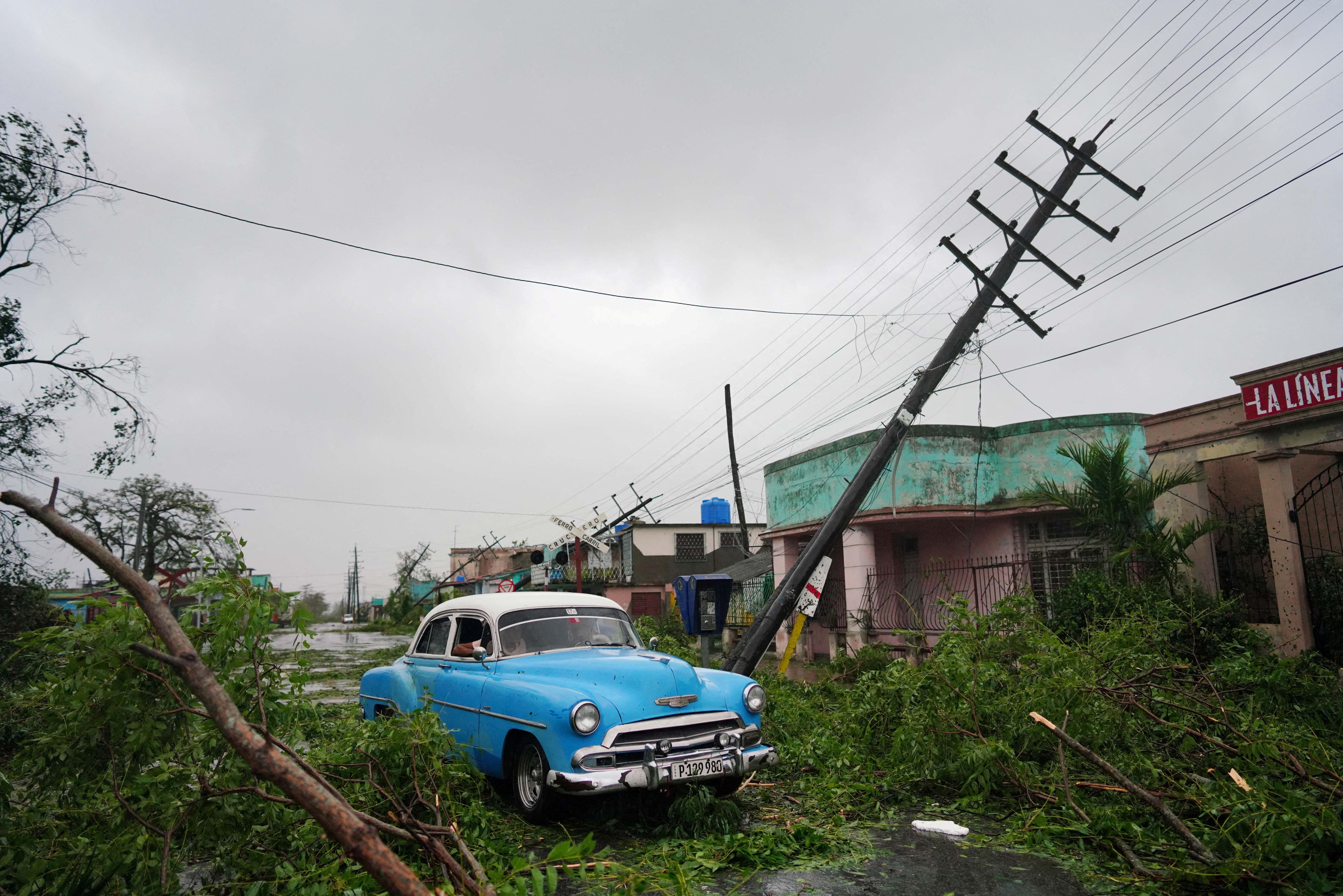 A vintage car passes by debris caused by the Hurricane Ian as it passed through Pinar del Rio, Cuba.