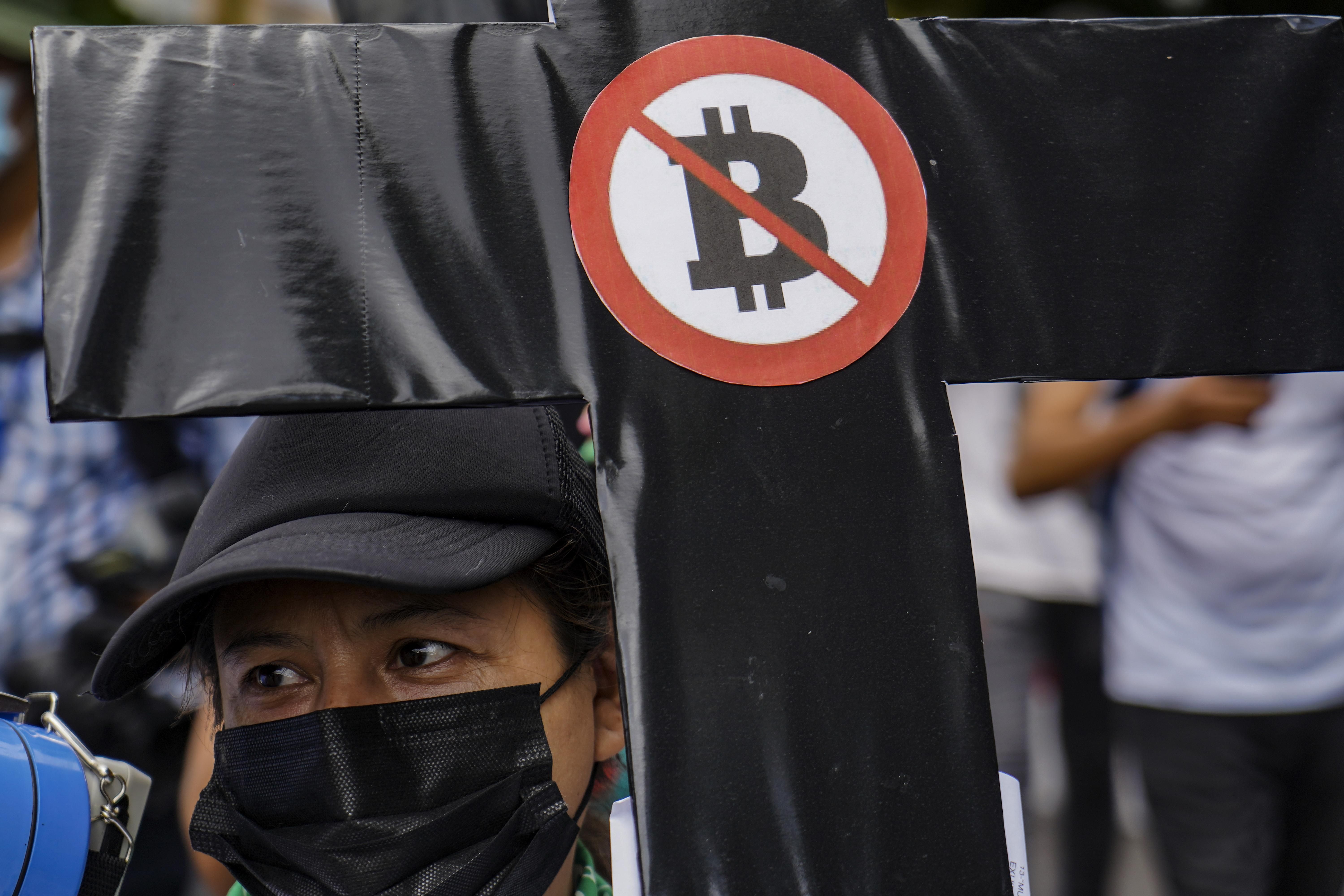 A woman holds a black cross with a sign against Bitcon during a protest against President Bukele's government in El Salvador. 