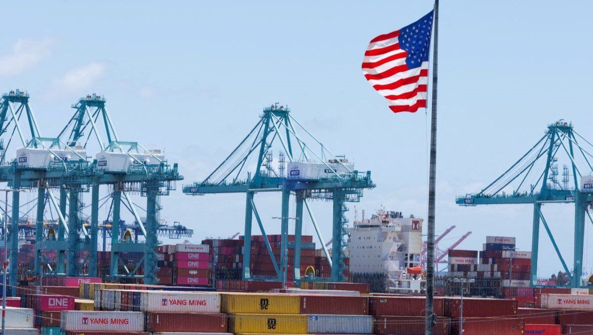 ​An American flag flutters over a ship and shipping containers at the Port of Los Angeles, in San Pedro California, U.S., May 13, 2025. 