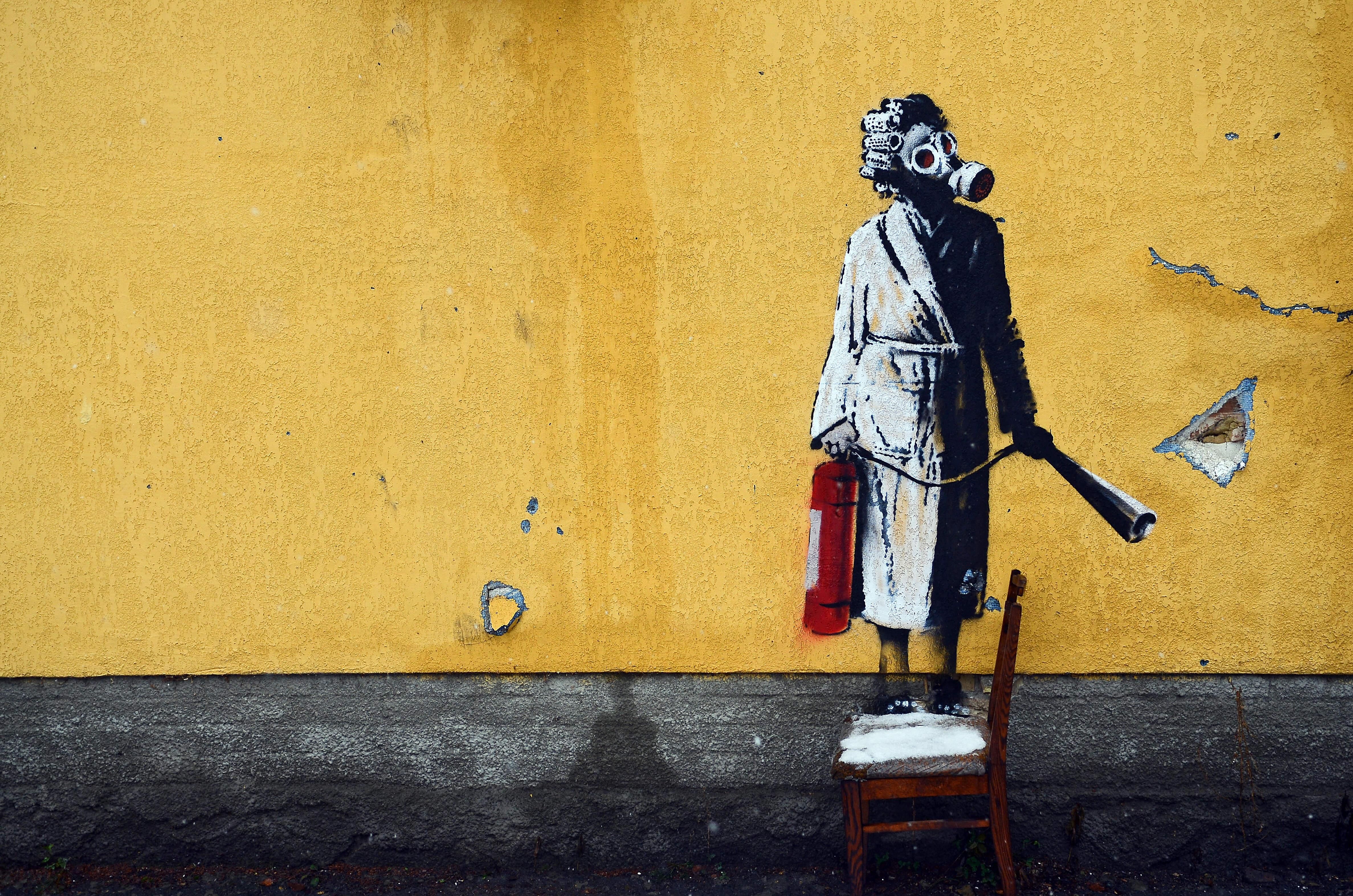 Banksy mural depicts a woman in a gas mask standing on a chair and holding a fire extinguisher in Hostomel, Ukraine.