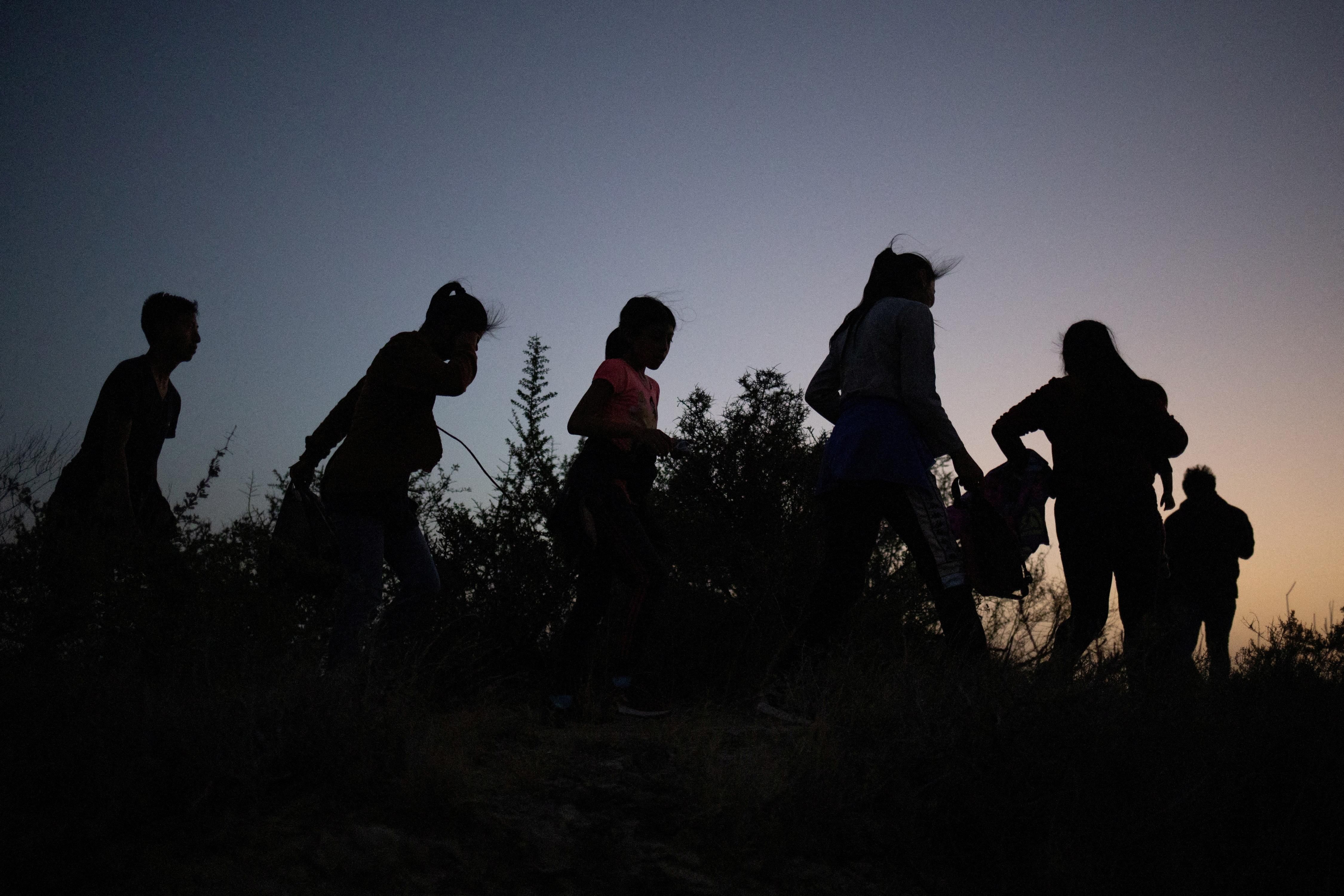 Migrants walk along a dirt trail after crossing the Rio Grande river into the US from Mexico in Roma, Texas.