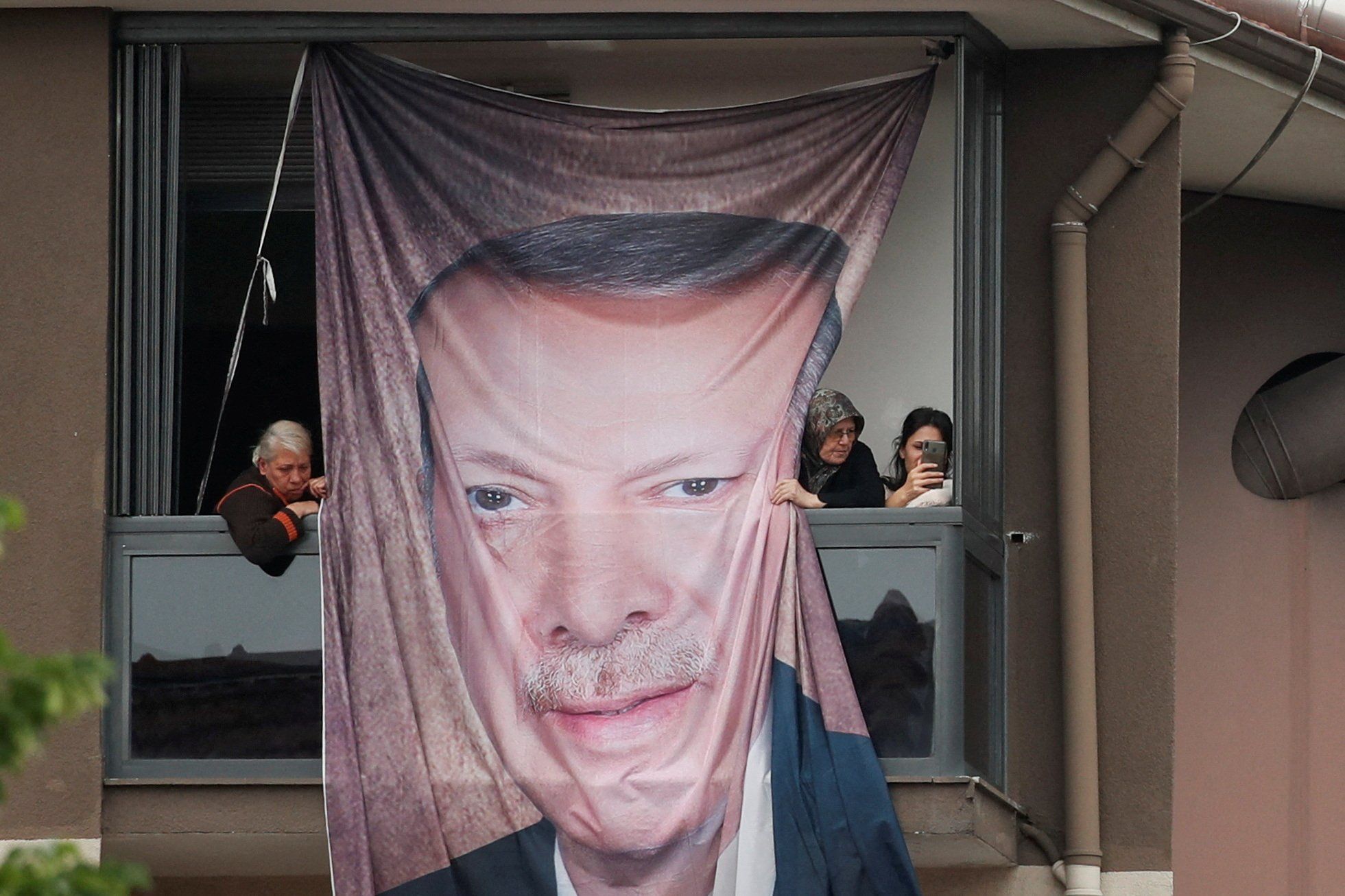 People look on from a balcony with a banner with the image of Turkish President Tayyip Erdogan. 